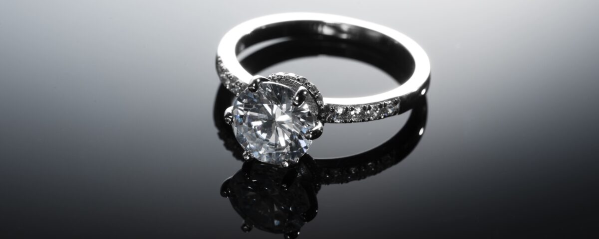 A stunning diamond engagement ring with a silver band placed on a reflective black surface, creating a luxurious and sophisticated look.