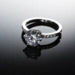 A stunning diamond engagement ring with a silver band placed on a reflective black surface, creating a luxurious and sophisticated look.