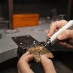 A skilled jeweler using a precision tool to solder a delicate gold chain, showcasing expert craftsmanship in handmade jewelry design.